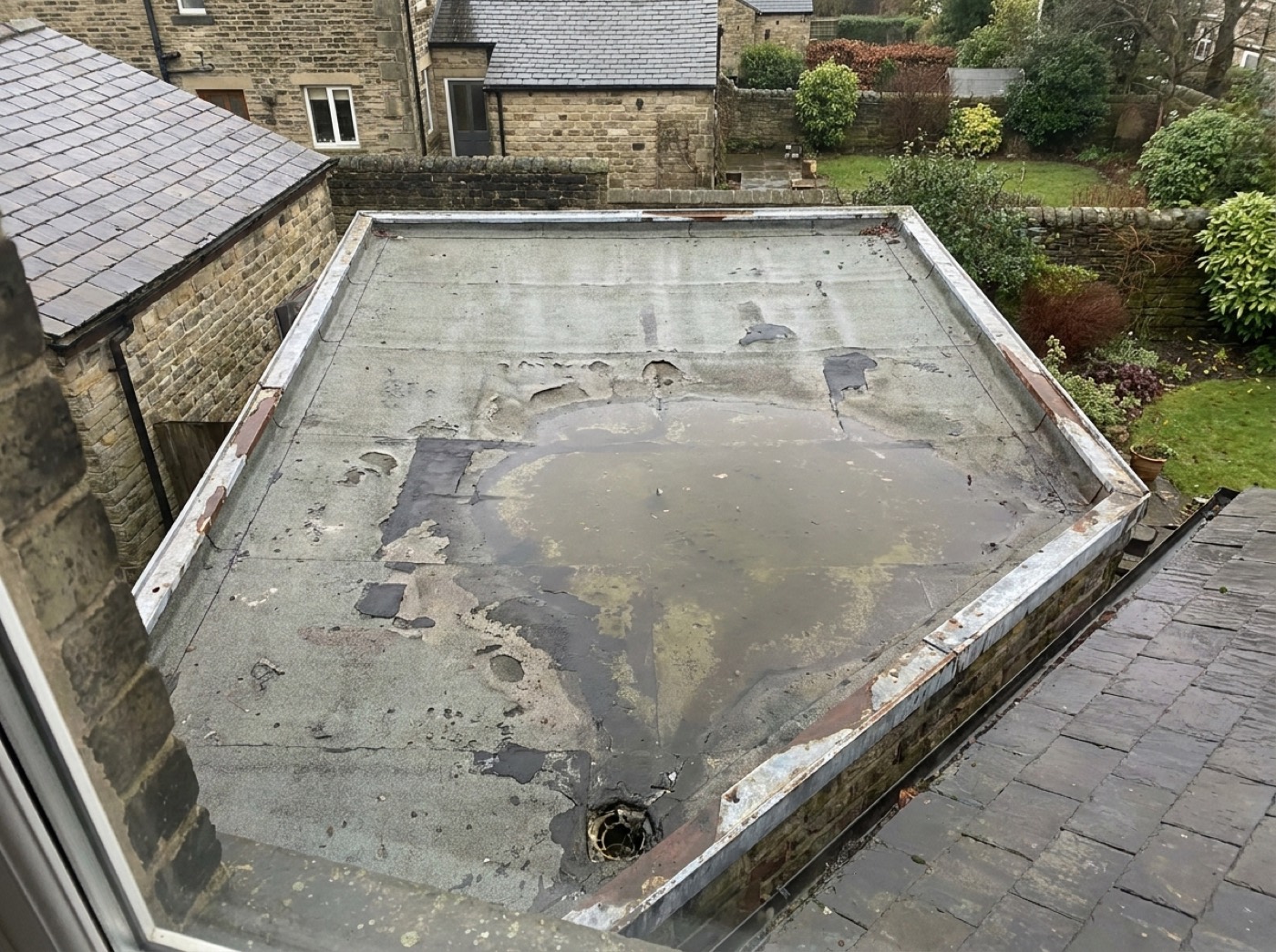 Blistered, patched felt on an extension roof with a pool of standing water and split edge trims